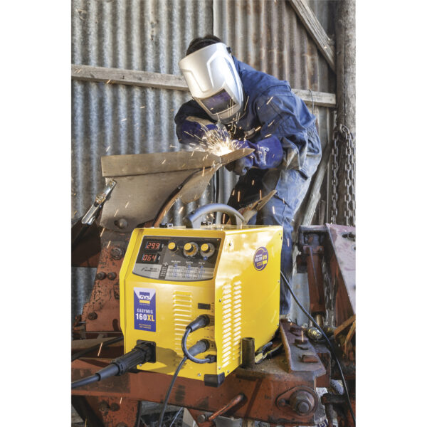 Person som bär skyddsutrustning medan han svetsar metall på en rostig, industriell maskin med gnistor som flyger; en GYS EasyMig 160 XL är i förgrunden.