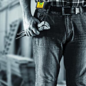 En person i jeans och rutig skjorta som håller i ett Fickvattenpass STABILA POCKET BASIC står i en industriverkstad.