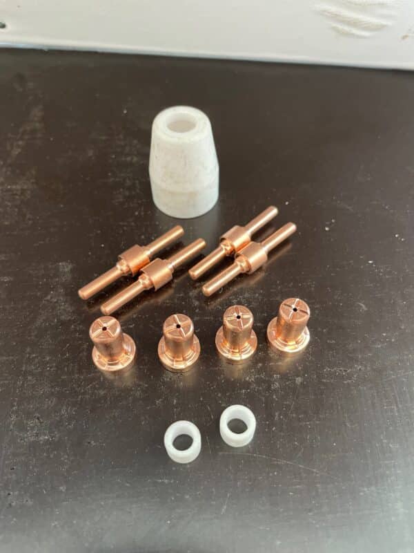 En samling av Slitdels-kit till PT31, passande bl a Lidl-plasman (ej B3-modellen) och två små vita plastringar är arrangerade på en mörk yta bredvid en större vit cylindrisk komponent.