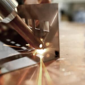 Närbild av ett metallstycke som svetsas med Hyr handhållen lasersvets Maxphotonics X1W-MFSC 1500, med ljusa gnistor och smält metall synlig vid svetspunkten. Rektangulära utskärningar ses på plåten.