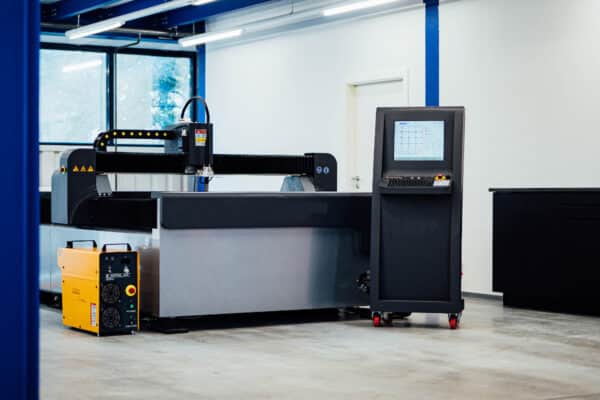 En stor Hugong 1,5 x 3 m Intecut-HT styrd plasma med vattenbord och dess kontrollenhet placeras i en rymlig, väl upplyst verkstad med blå överliggande strukturer och ett fönster.