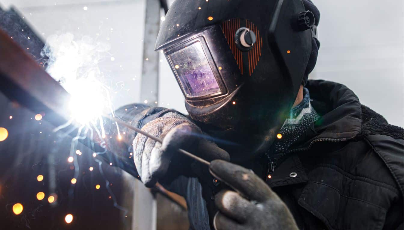 en svetsare med svetshjälm och skyddshandskar svetsar metall