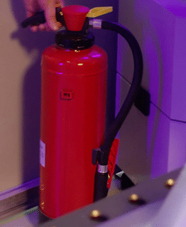 en röd brandsläckare ställs ner i ett hörn vid ett svetsbord