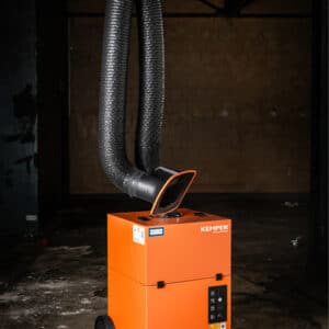 Kemper mobilt rökutsug SmartMaster är en industriorange luftfiltreringsenhet på hjul med en flexibel svart utblåsningsslang som sträcker sig uppåt, i ett svagt upplyst, oavslutat rum med betonggolv och betongväggar.